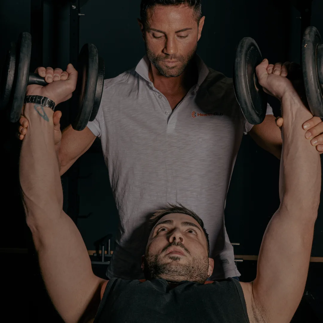 Personal trainer assiste panca con manubri Carpi